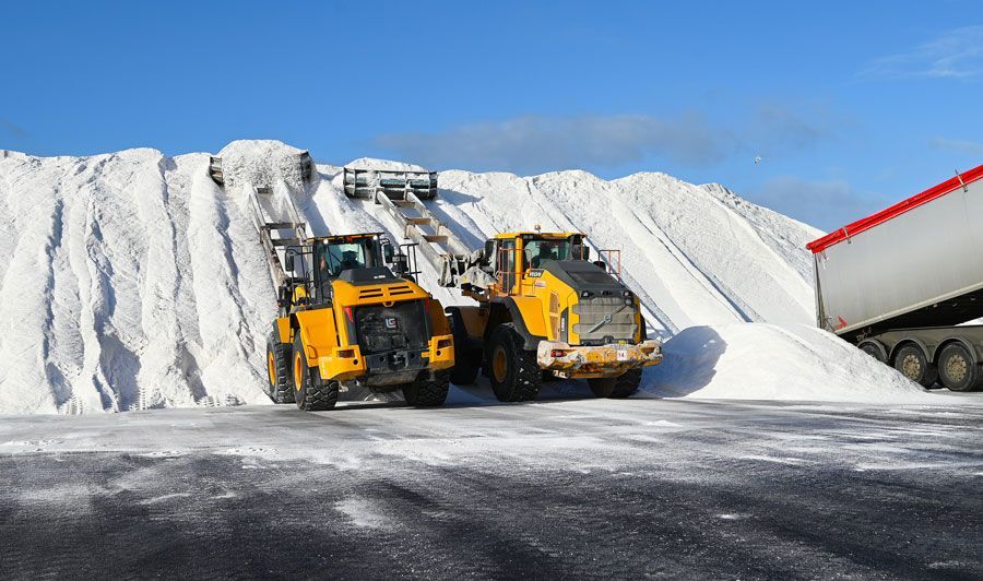 Chargeurs jaunes dans une installation de stockage de sel, avec des camions et un énorme tas de sel blanc sous un ciel bleu.