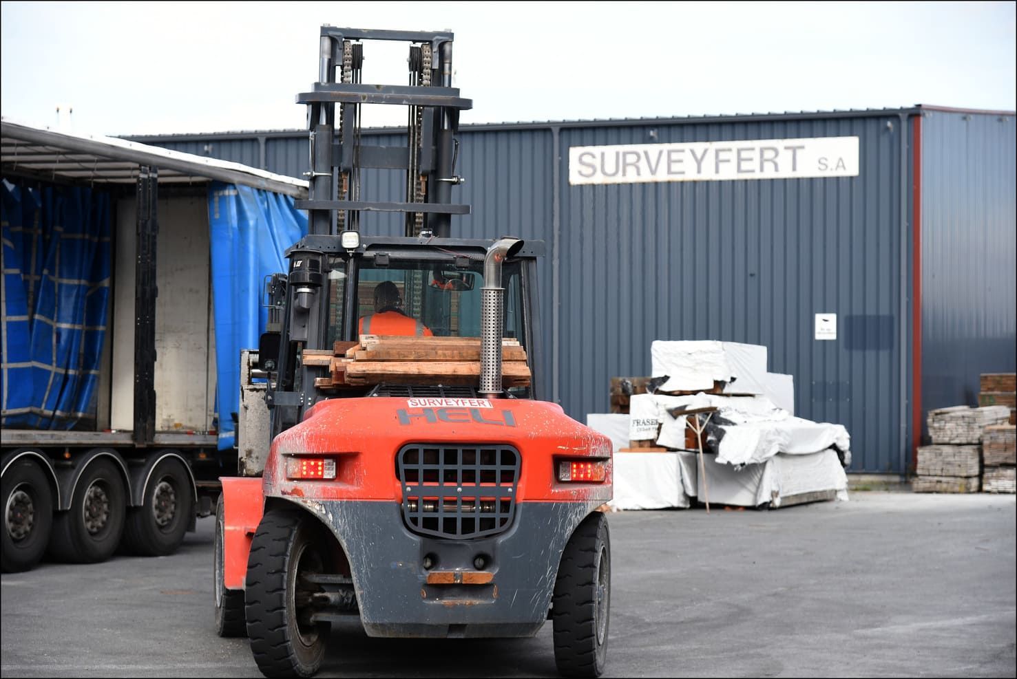 Chariot élévateur rouge chargeant une cargaison près du bâtiment SURVEYFERT.