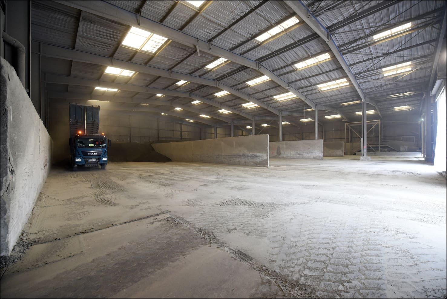 Intérieur d'entrepôt avec un camion, des piles de matériaux et des plafonniers.