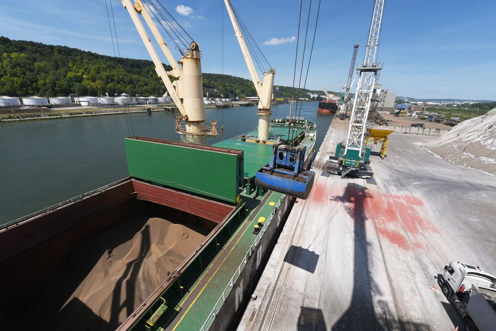Cargo en cours de chargement dans un port, avec des grues, des véhicules et des réservoirs de stockage.