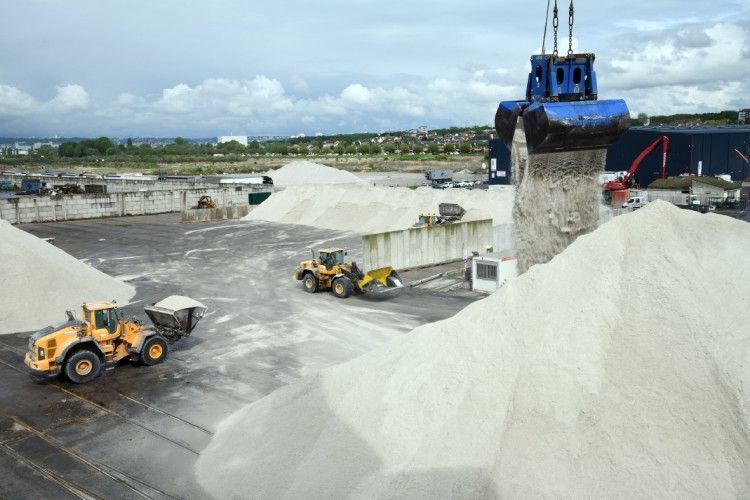 Deux chargeurs jaunes déplacent du matériel blanc dans une cour industrielle ; une grue bleue est au-dessus.