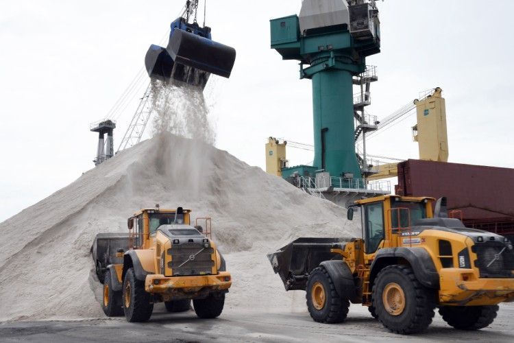 Deux chargeurs jaunes dans un port, déchargeant une montagne de sable d'une grue.