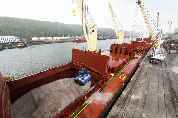 Navire cargo chargé de matériaux sur un quai, avec des grues et une cale remplie.