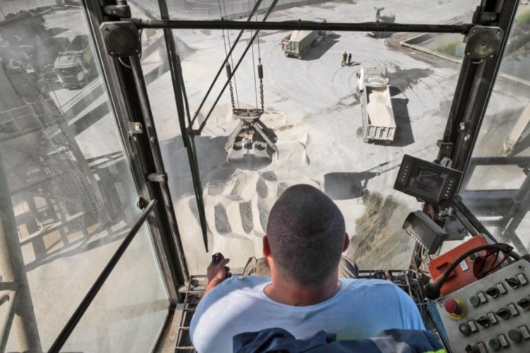 Personne opérant une grue, chargeant du sable dans une carrière ; vue depuis l'intérieur de la cabine de la grue.