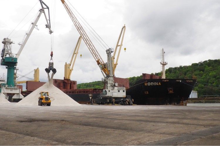 Un cargo est chargé d'une substance blanche par des grues dans un port, avec un petit véhicule jaune.