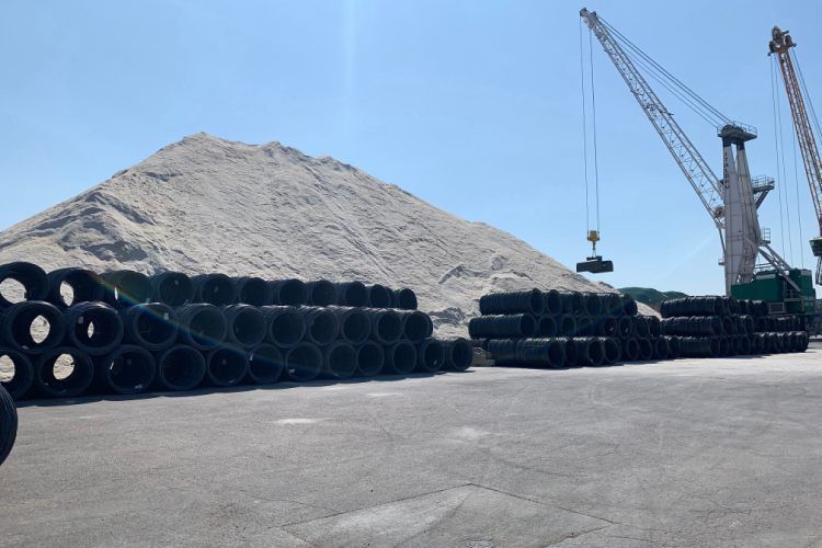 Pneus empilés sur un quai près d'un gros tas de matériaux et de grues sous un ciel bleu.
