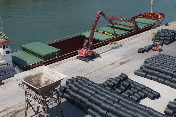 Un cargo à quai est chargé de bobines d'acier noir. Grue rouge.