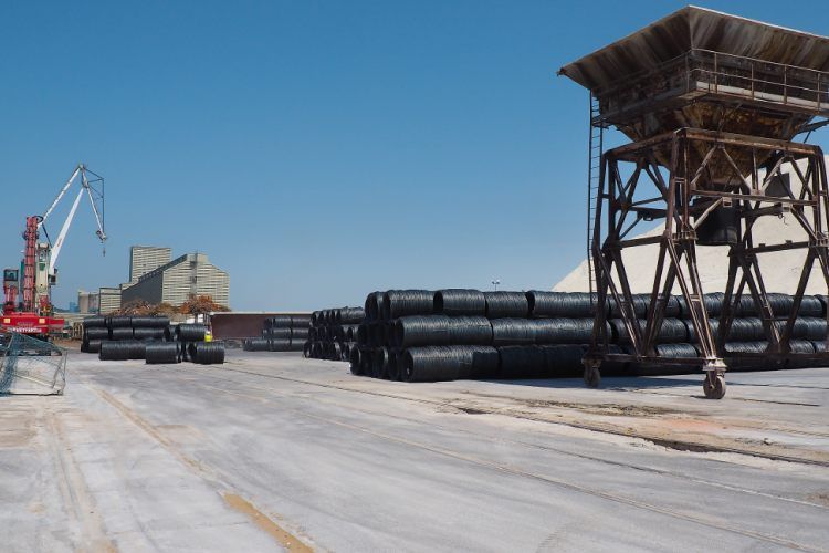 Scène de port industriel avec rouleaux de fil noir, grue, tour et ciel clair.