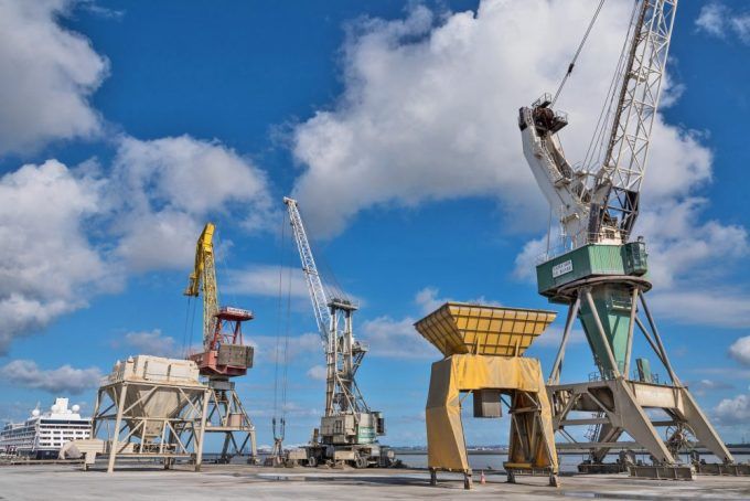 Grues dans un port avec un ciel nuageux et un bateau de croisière en arrière-plan.