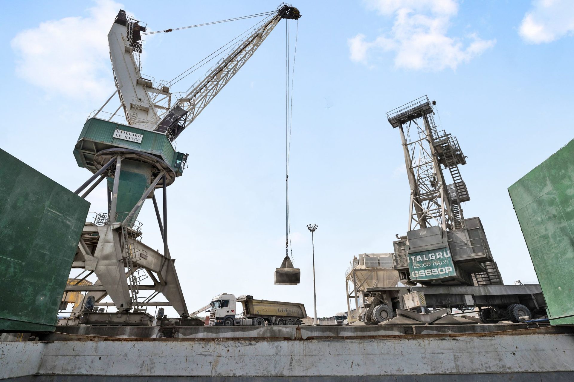 Grues chargeant des marchandises dans un port. Une grue dépose un conteneur sur un camion. Ciel en arrière-plan.