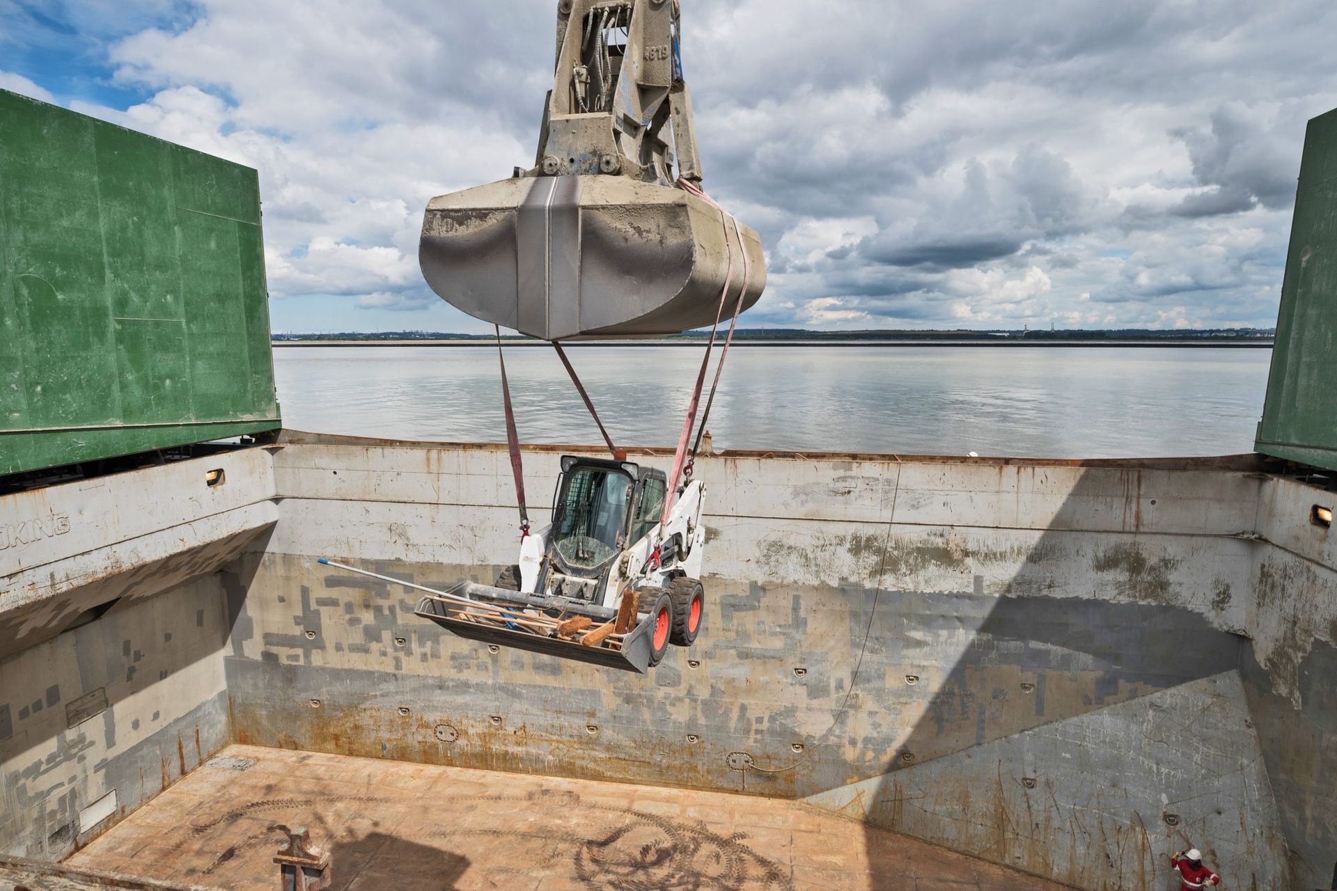 Une grande grue soulevant une chargeuse compacte Bobcat de la cale d'un navire.
