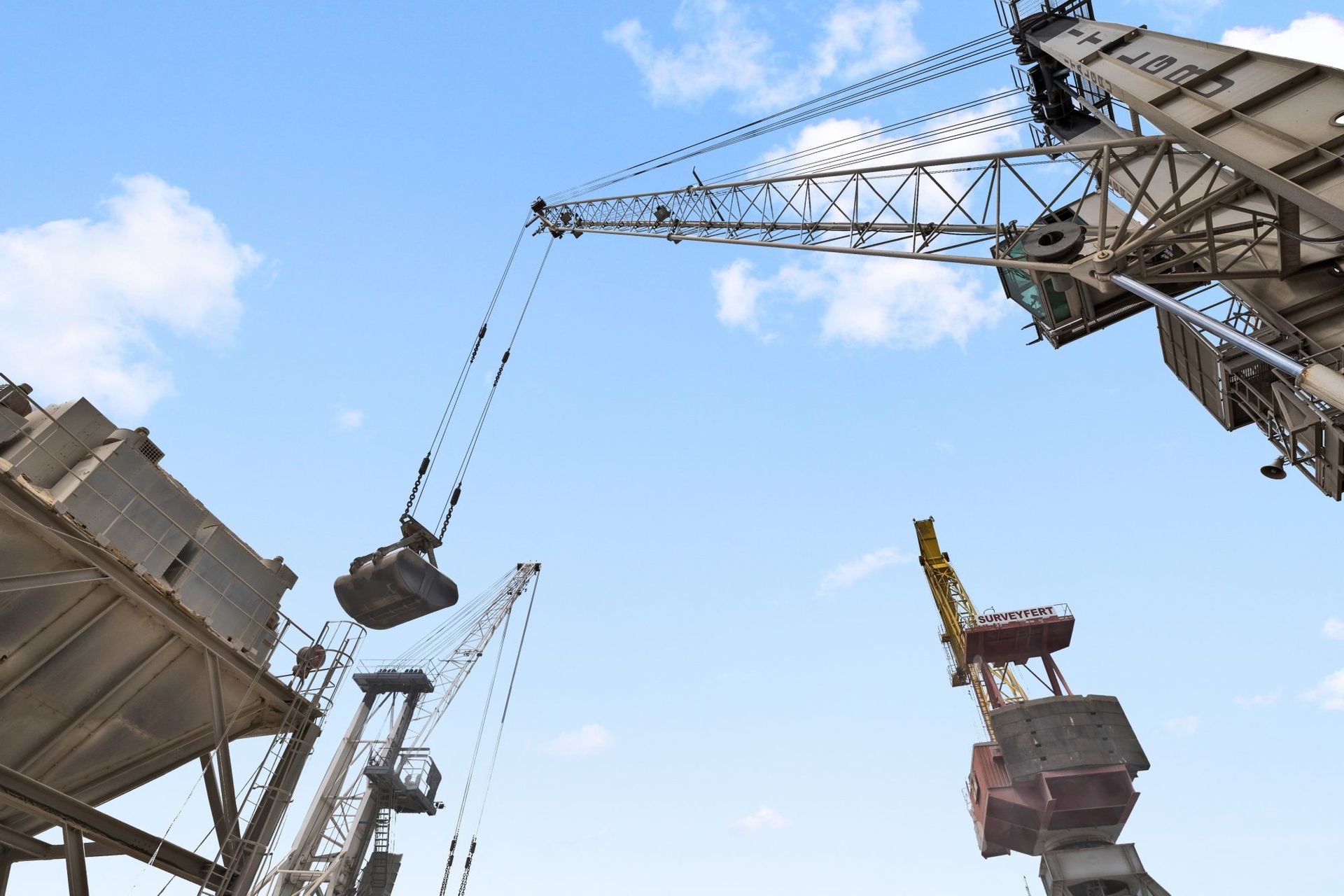 Grues soulevant des marchandises dans un port, contre un ciel bleu vif.