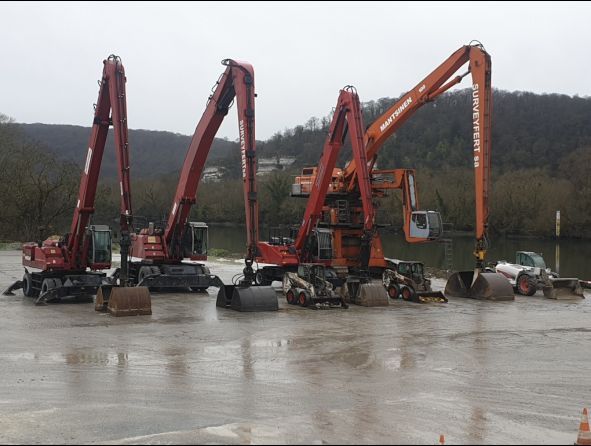 Des excavatrices stationnées près d'une colline boisée.