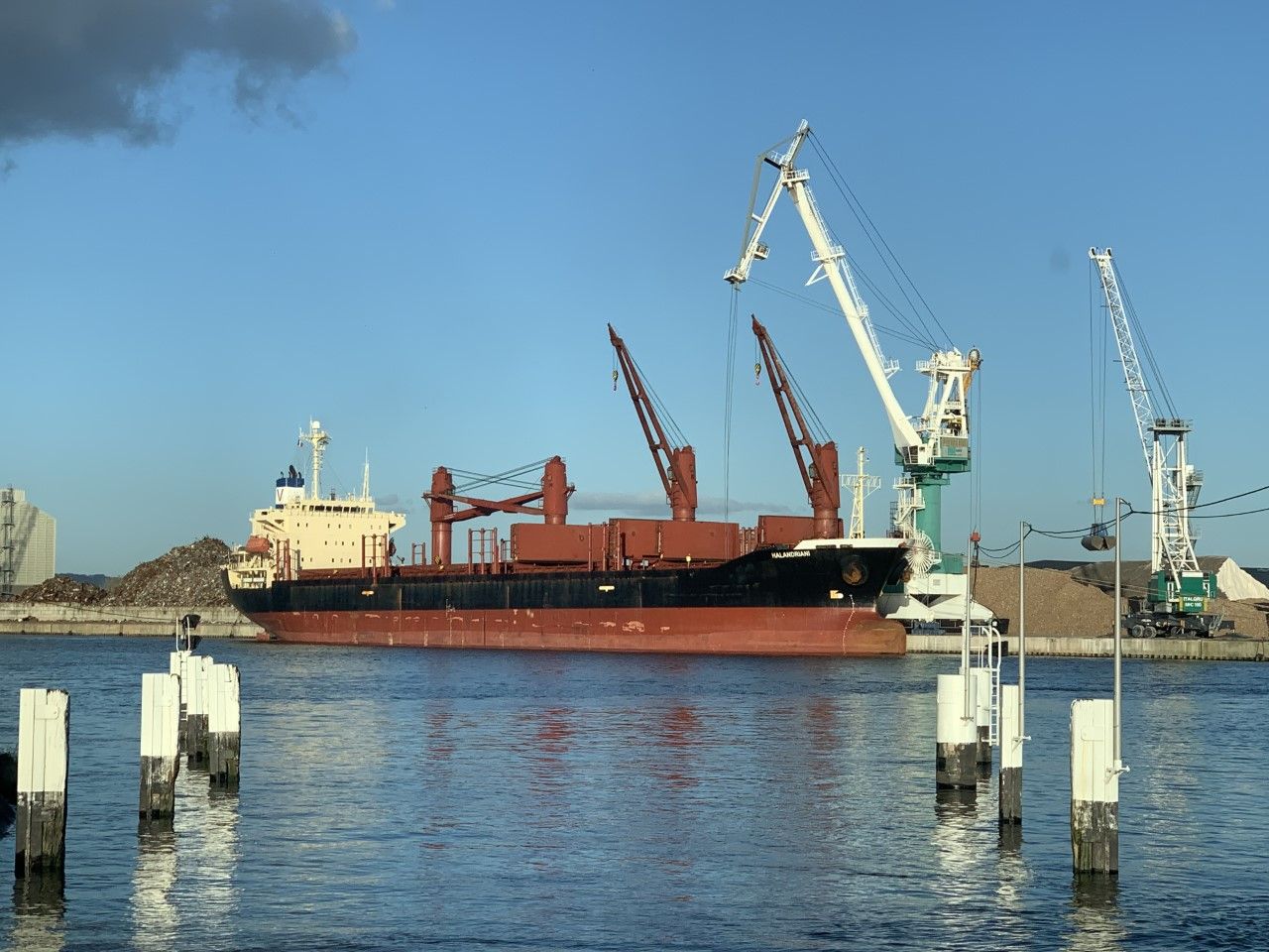 Un cargo est chargé dans un port avec des grues sous un ciel bleu.