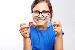 Una joven que lleva gafas sostiene dos aparatos ortopédicos en sus manos.