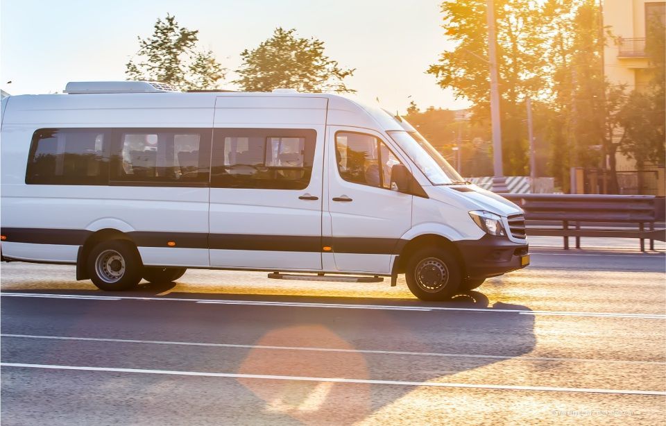 Ein weißer Kleinbus fährt bei Sonnenuntergang auf einer sonnenbeschienenen Straße.
