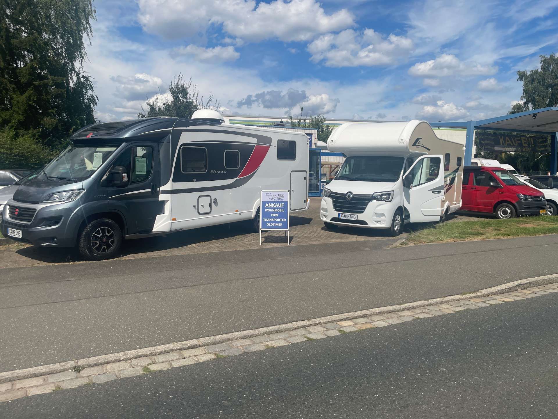 Wohnmobile parkten auf einem Parkplatz neben einer Straße unter bewölktem Himmel, davor stand ein kleines Schild.