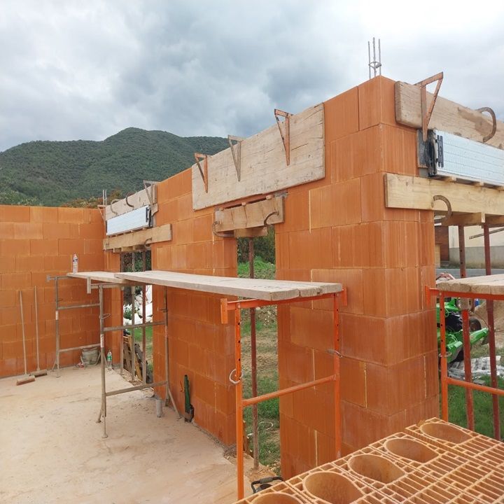 Chantier : murs de briques orange avec échafaudages et poutres de soutien.