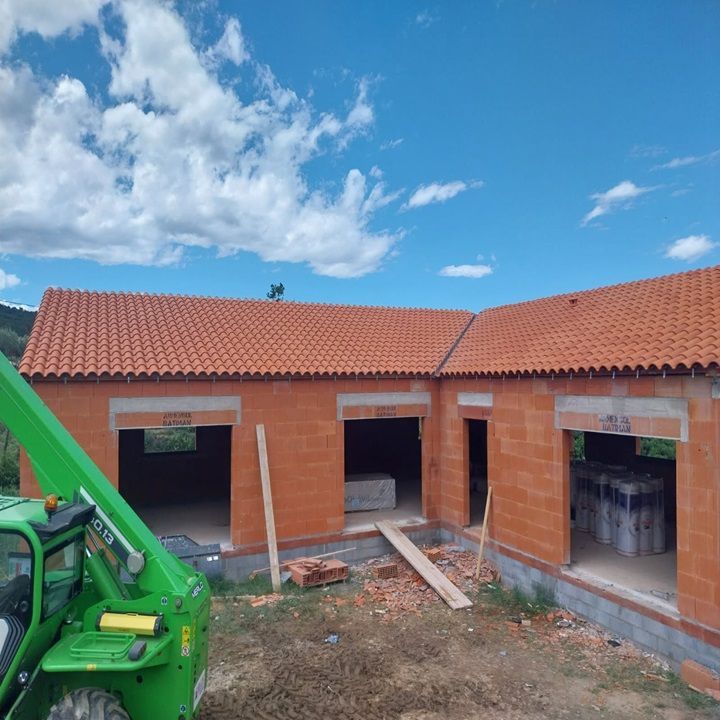 Bâtiment en construction, toit de tuiles rouges, murs de briques orange.