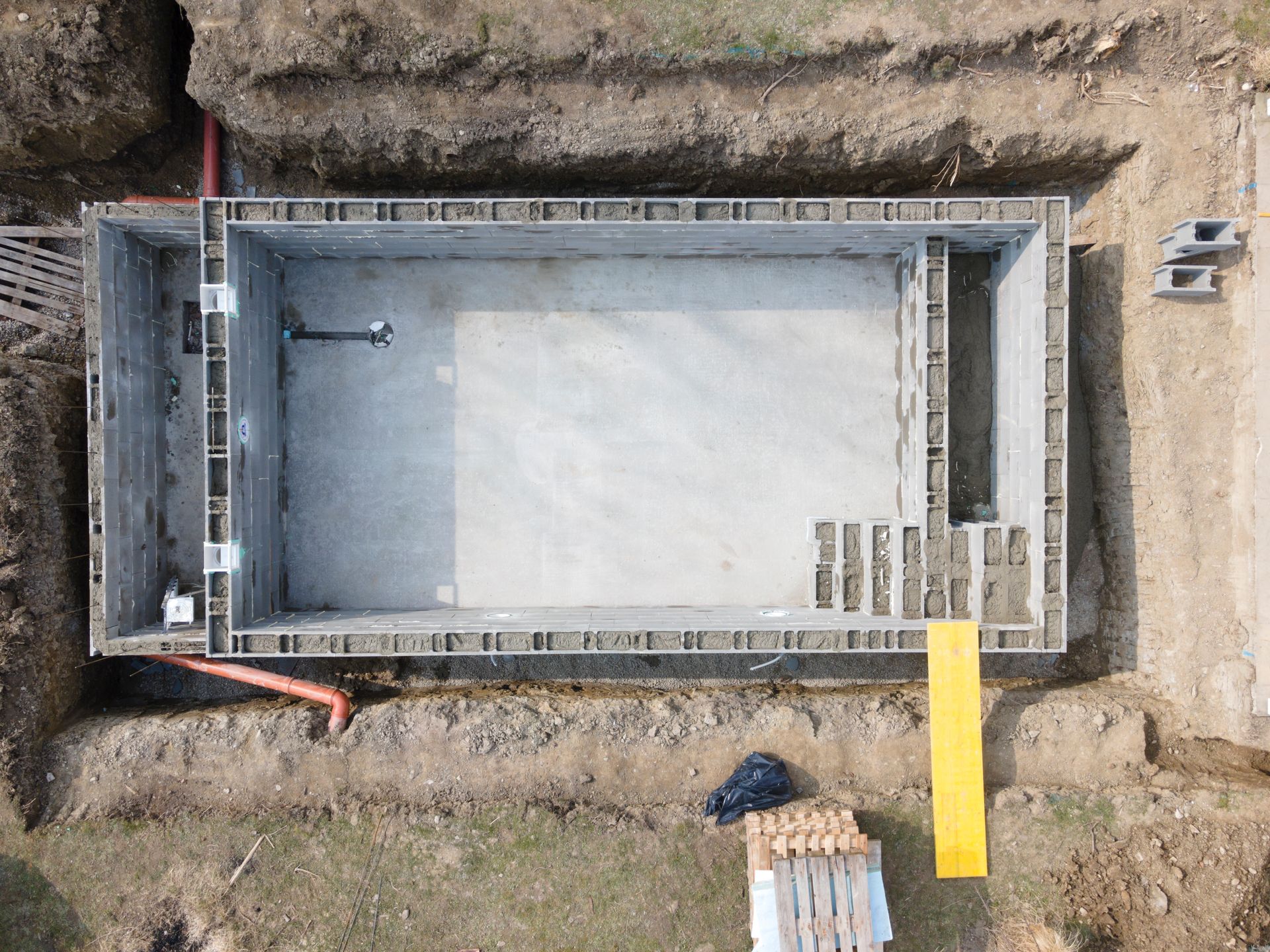 Vue aérienne d'une coque de piscine rectangulaire en béton en construction, dans une excavation.