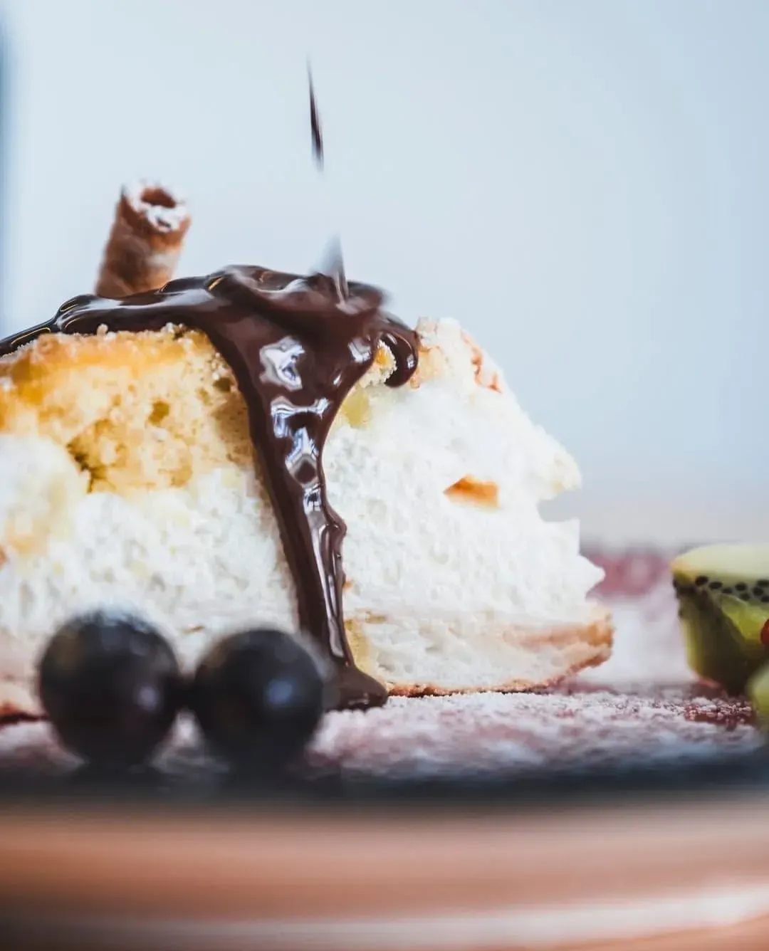 Una porción de pastel cubierta con crema batida, rociada con chocolate y adornada con uvas y kiwi.