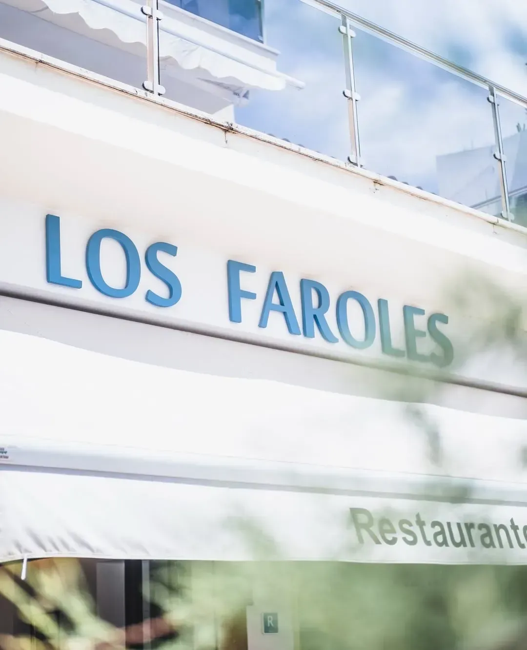 El letrero del restaurante Los Faroles presenta texto azul sobre una fachada blanca con barandillas de balcón en la parte superior.
