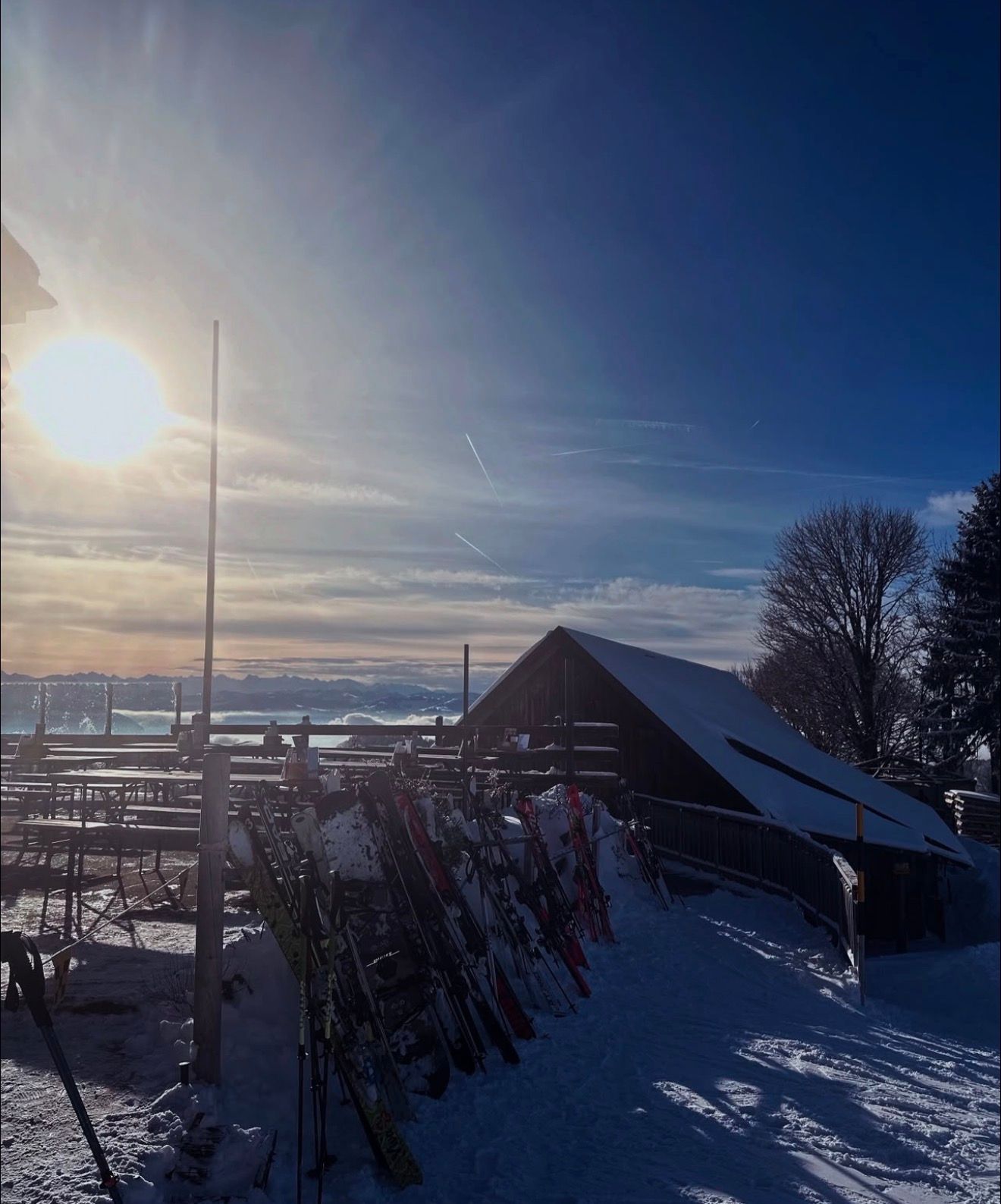 Verschneites Skigebiet bei Sonnenaufgang, Skier stehen unter strahlend blauem Winterhimmel neben einem kleinen Gebäude.