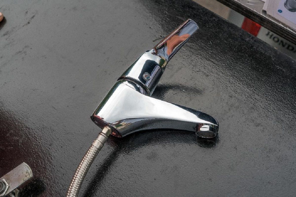 Un robinet de salle de bain chromé à poignée unique, posé sur une surface sombre et humide, avec un tuyau métallique raccordé.