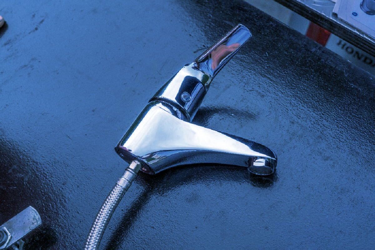 Un robinet chromé à poignée unique, muni d'un tuyau métallique flexible, posé sur une surface sombre.