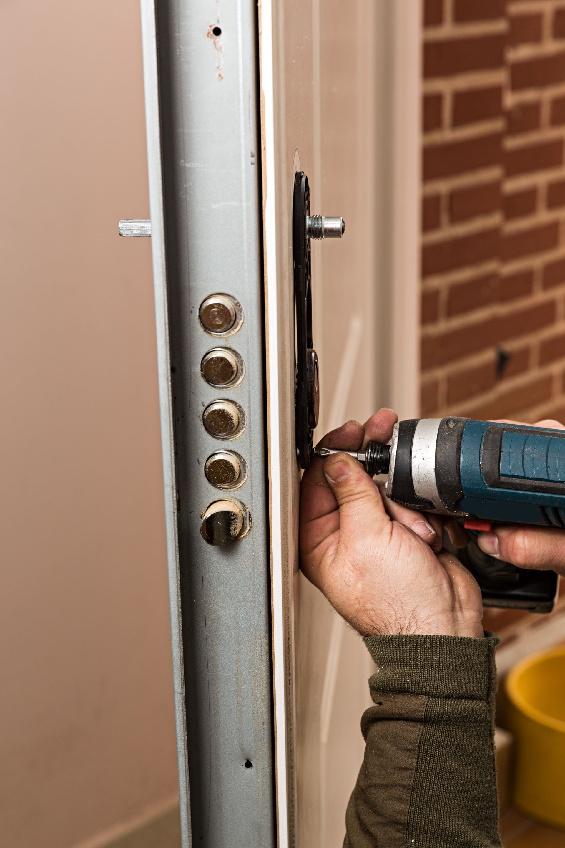 Gros plan sur des mains utilisant une perceuse électrique pour installer une serrure de sécurité sur le côté d'une porte blanche.