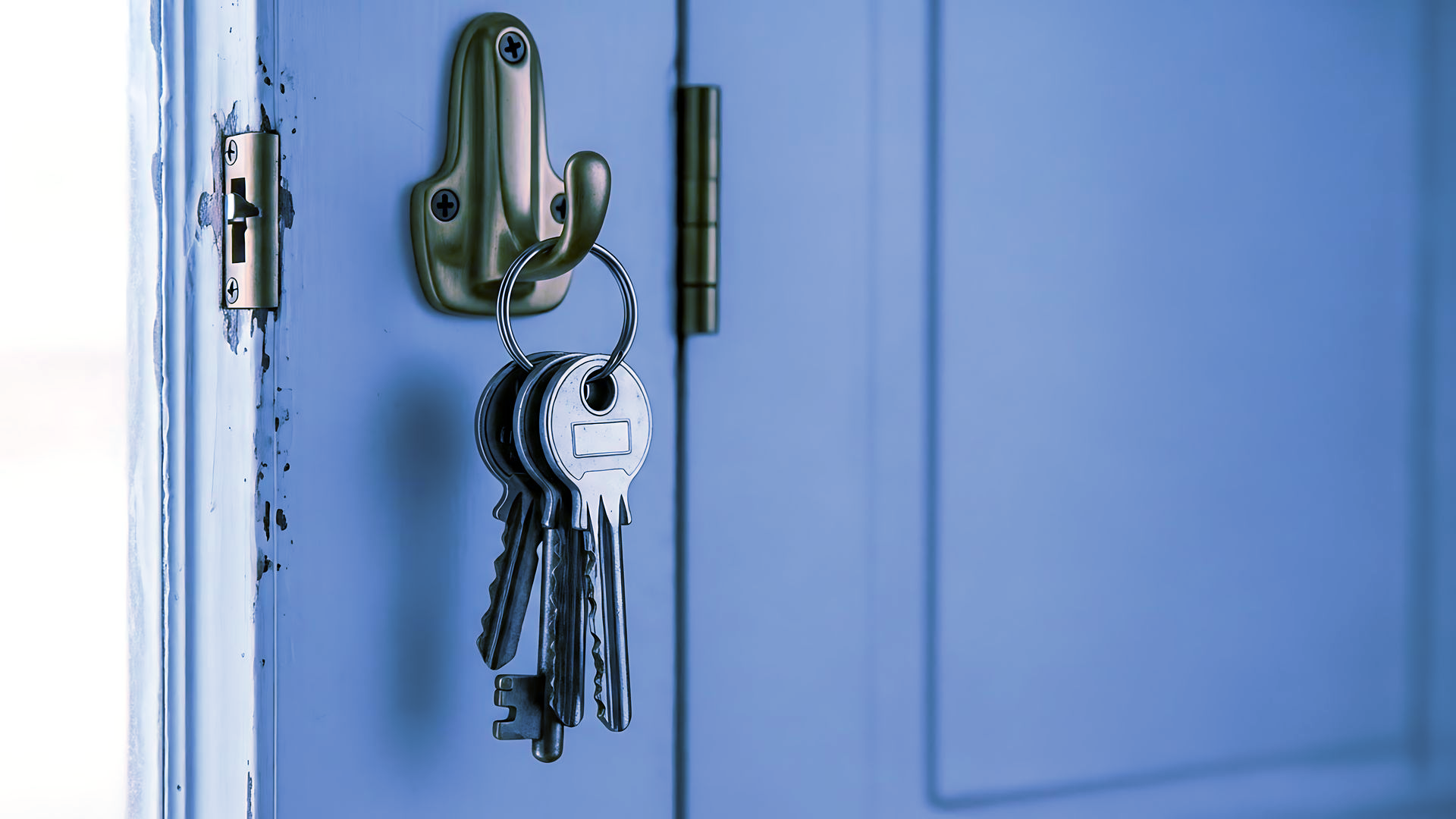 Un anneau métallique de clés suspendu à un crochet mural argenté sur un cadre de porte bleu clair.
