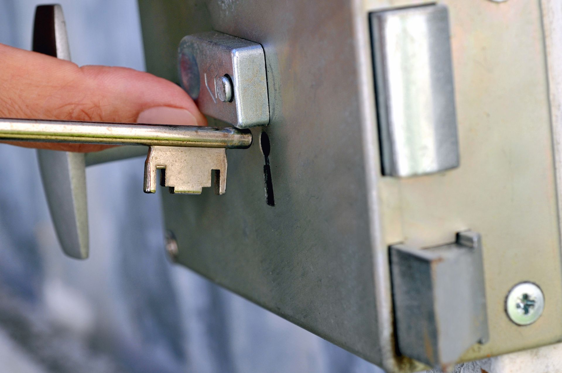 Une main tient une clé métallique et l'insère dans la serrure d'un mécanisme de porte.