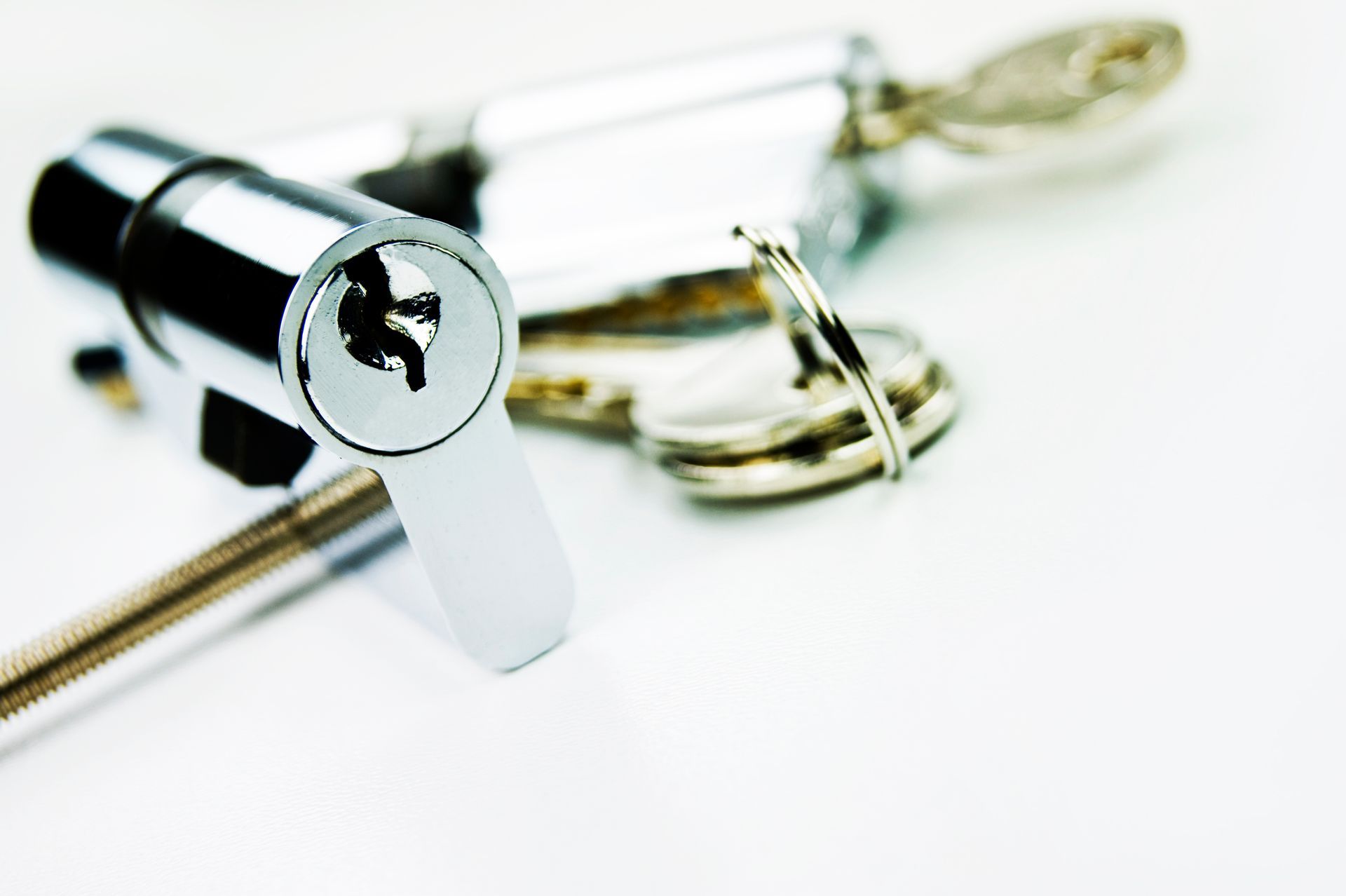 Gros plan sur un mécanisme de serrure à cylindre argenté et un porte-clés à plusieurs clés posés sur une surface blanche.