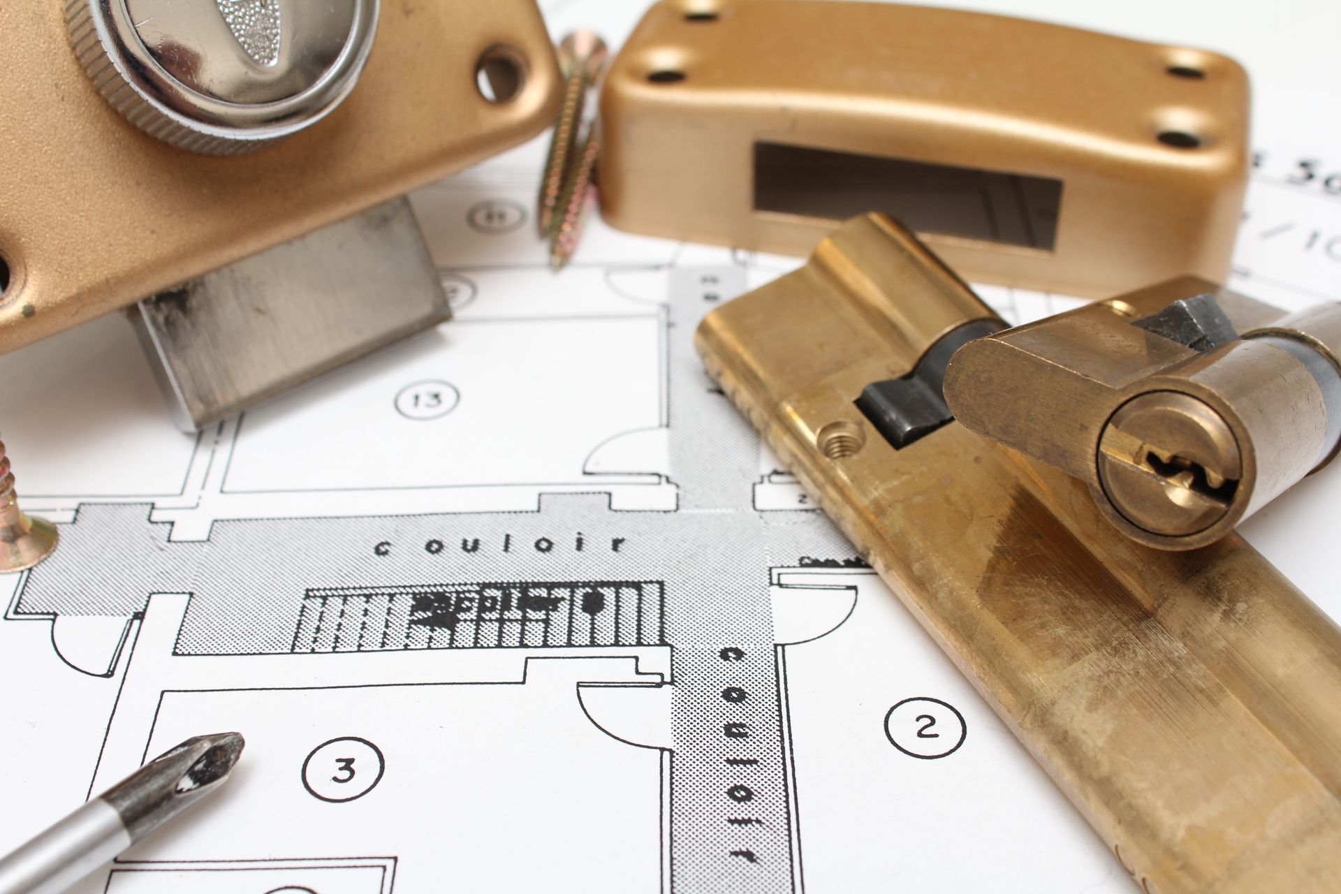 Des serrures de porte en laiton et un tournevis posés sur un plan architectural imprimé.
