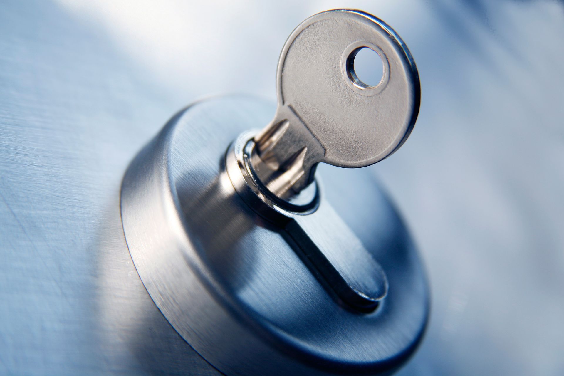 Une clé argentée insérée dans une serrure de porte métallique circulaire, photographiée en gros plan.