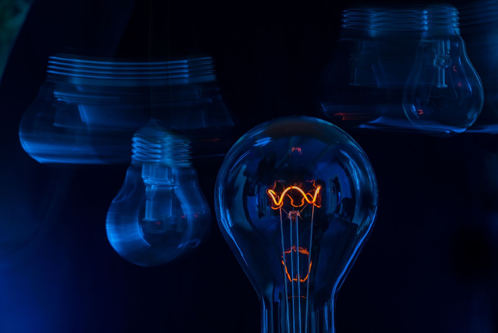 Une ampoule unique et lumineuse, avec un filament orange visible, entourée d'ampoules à la lumière tamisée et floue, dans une pièce sombre.