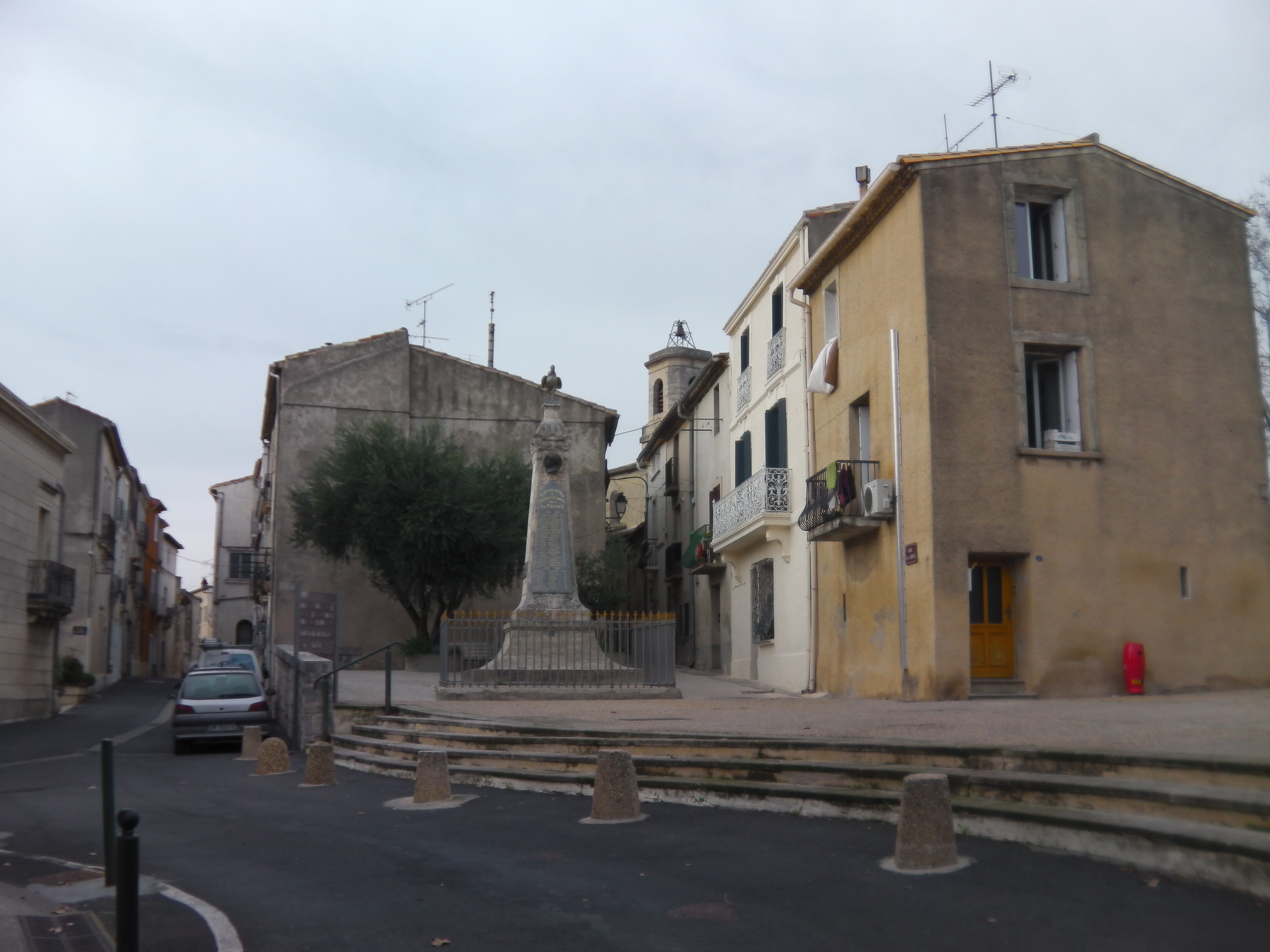 Un monument de pierre se dresse sur une place de la ville, entouré de vieux bâtiments, sous un ciel nuageux.