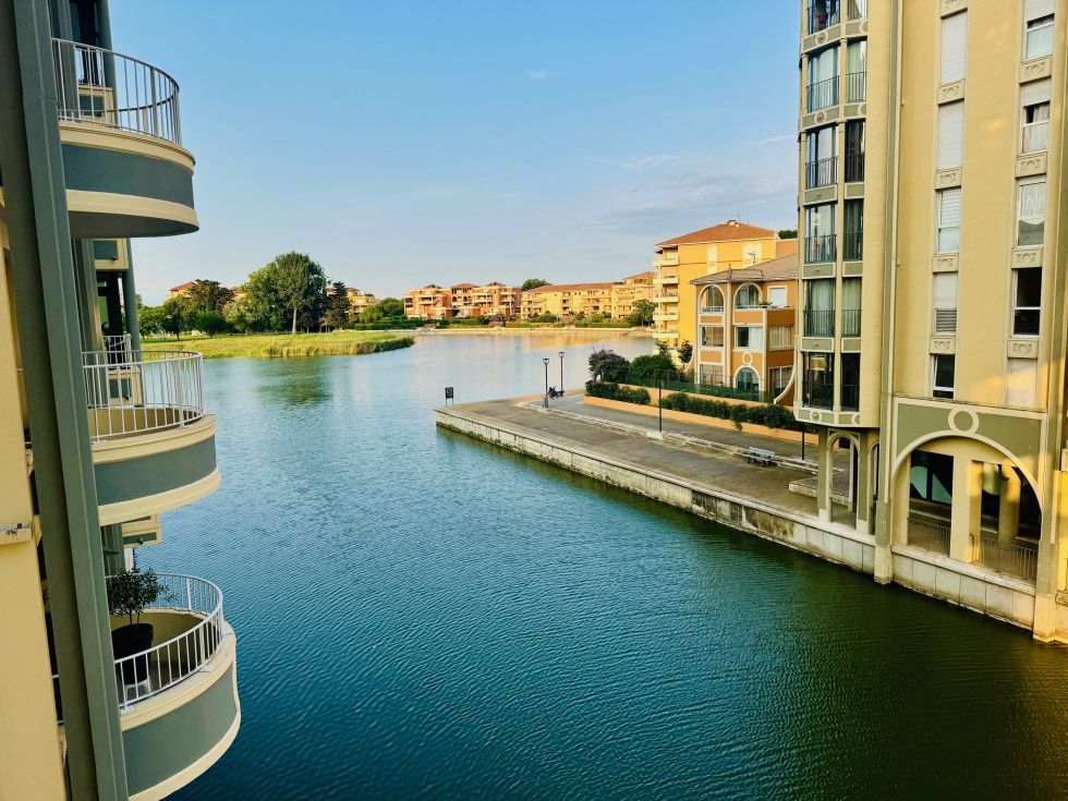 Un canal paisible serpente entre des immeubles d'appartements modernes sous un ciel d'un bleu limpide, avec un chemin piétonnier pavé au loin.