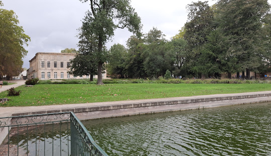 Un monument de pierre se dresse sur une place de la ville, entouré de vieux bâtiments, sous un ciel nuageux.
