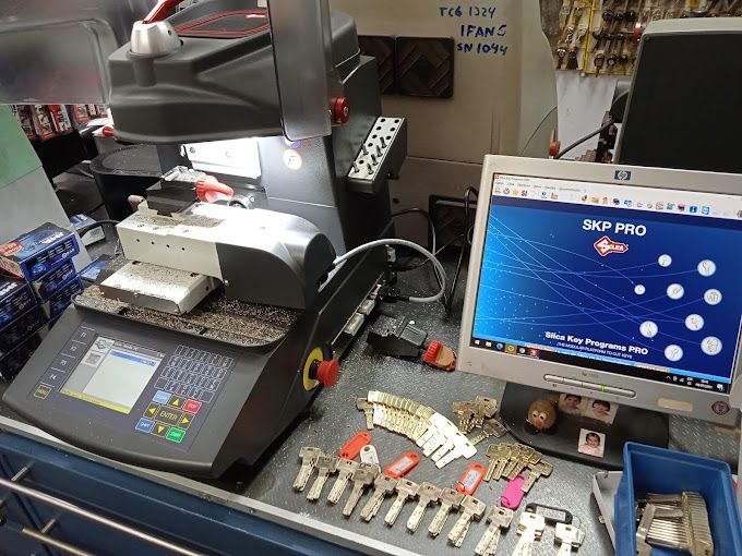 Una máquina cortadora de llaves está sobre un mostrador al lado de un monitor de computadora.