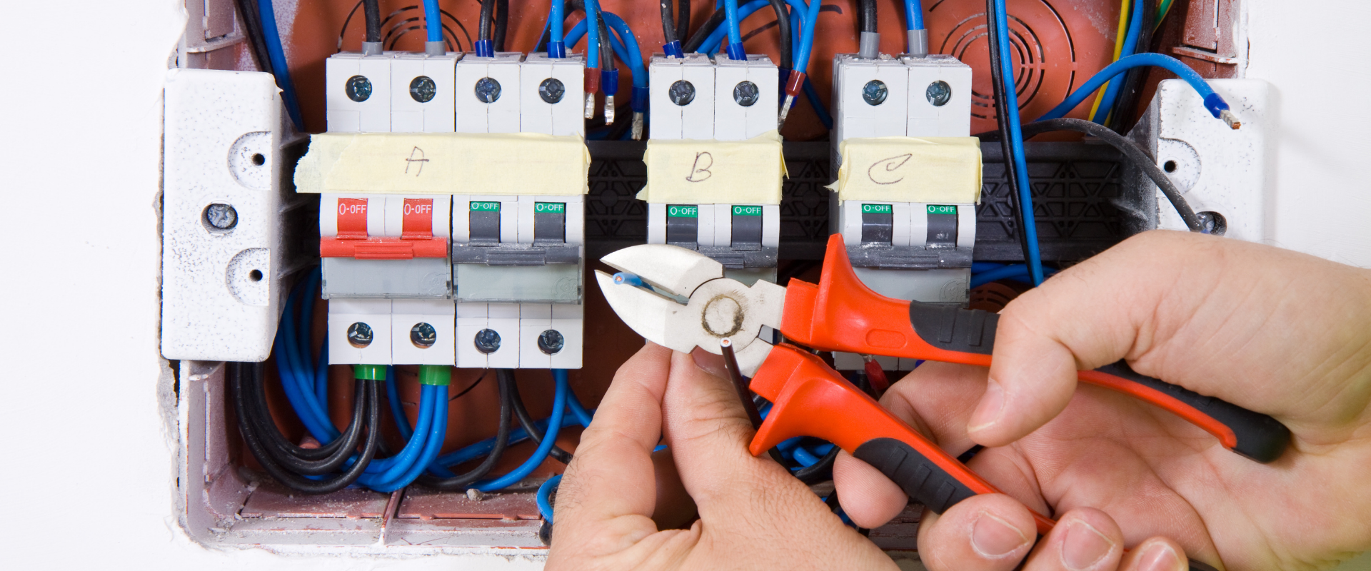 Une personne utilise une pince sur des câbles électriques dans un tableau électrique.
