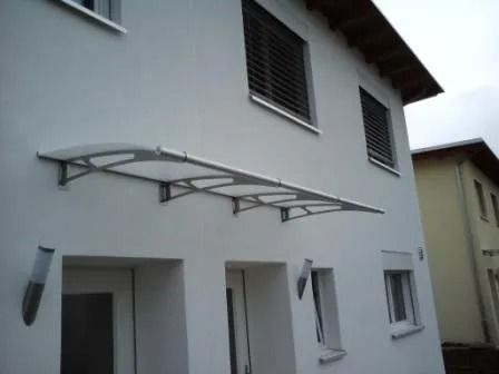 Weisses Haus mit silberner Markise über der Eingangstür, drei Fenstern und Wandleuchten.