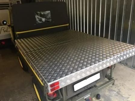 Ein Pritschenwagen mit einer Ladefläche aus gerändeltem Aluminium, einem schwarzen Stoffverdeck und roten Rückleuchten.