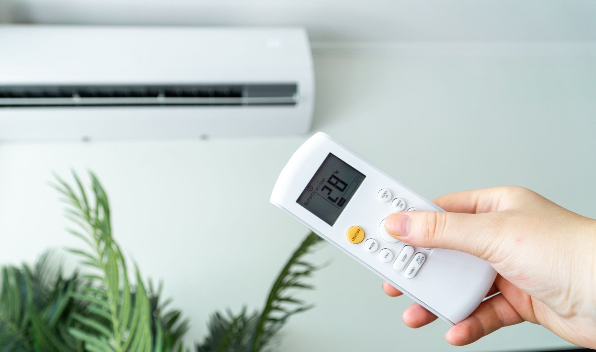 Main tenant la télécommande, réglant le climatiseur sur 28 degrés.