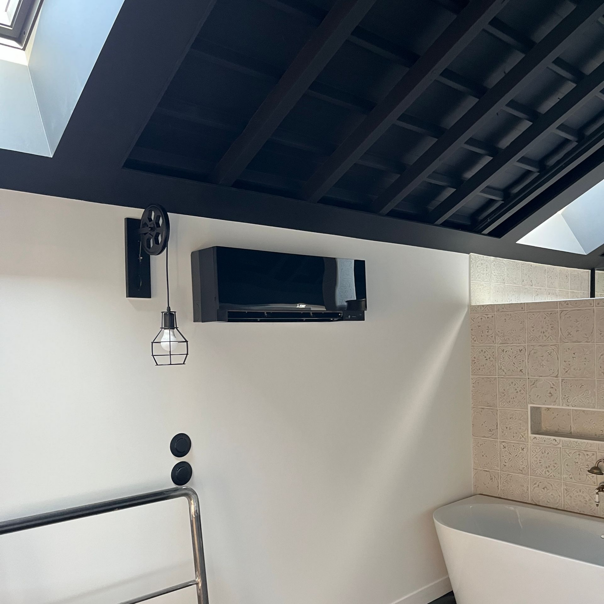 Salle de bains moderne avec climatisation noire murale, baignoire et mur carrelé texturé.