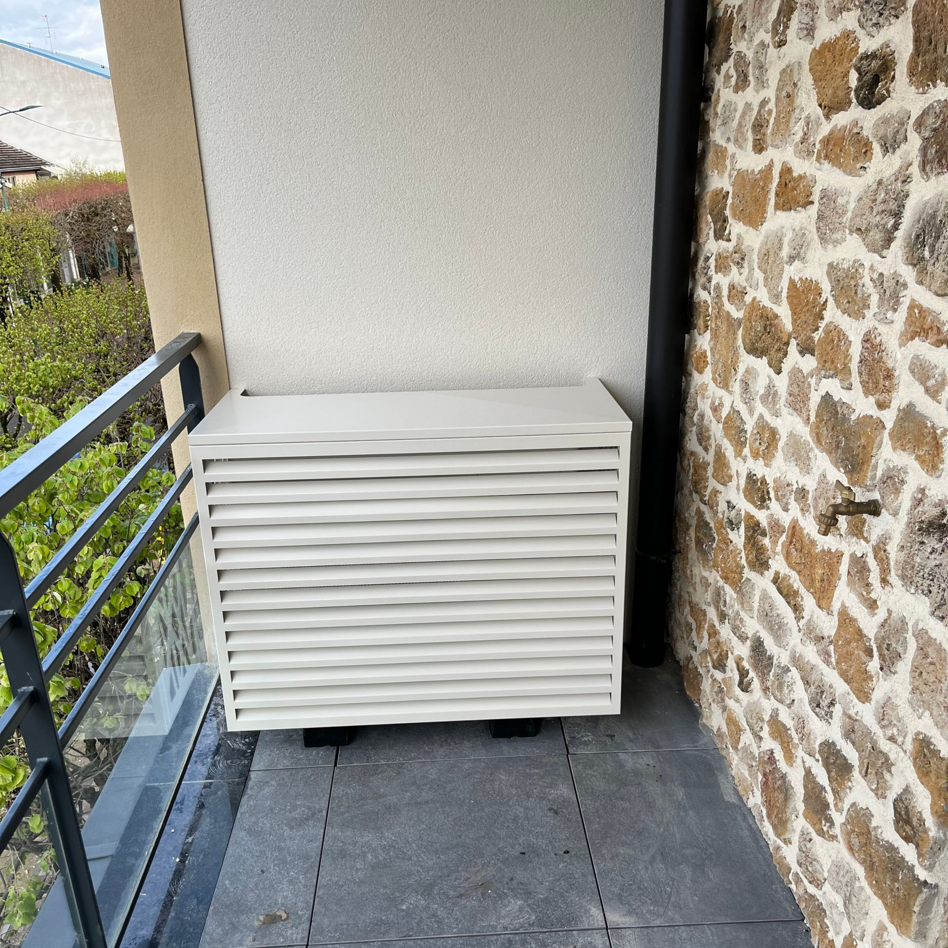 Climatiseur beige à persiennes sur un balcon.