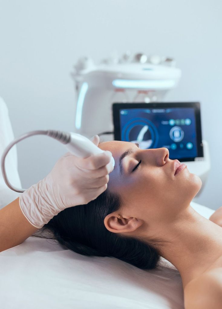 Mujer recibiendo tratamiento facial; técnico utilizando dispositivo en la frente.