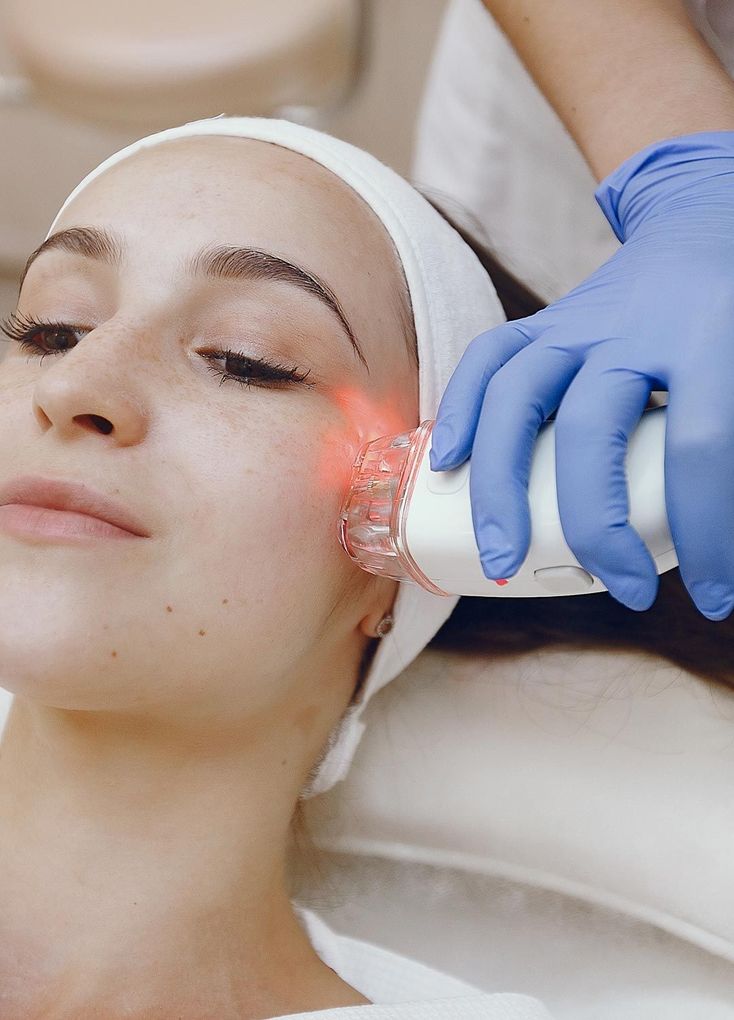 Mujer recibiendo tratamiento facial con un dispositivo de luz roja. Una persona con guantes sostiene el dispositivo.