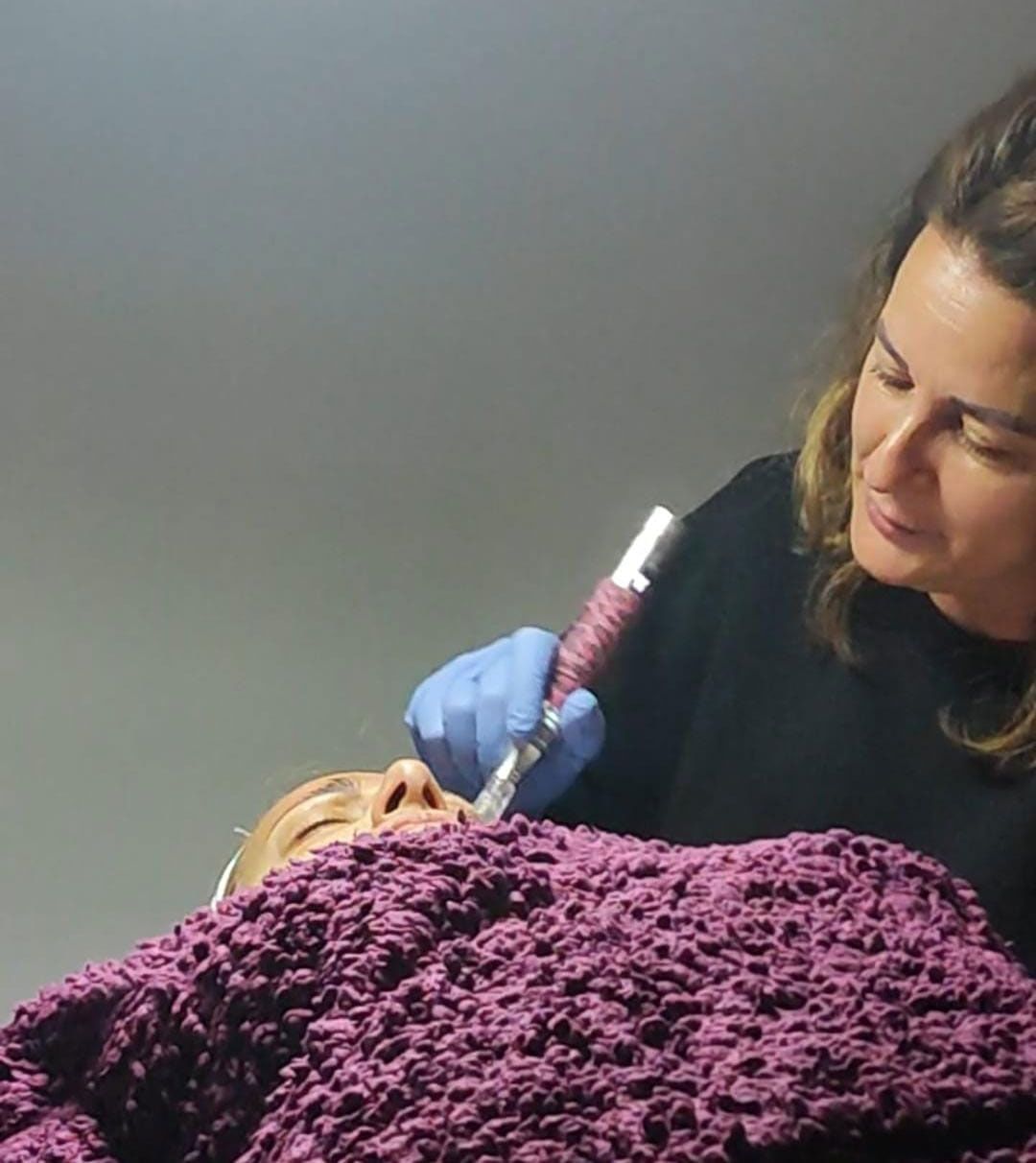 Una mujer sostiene una jeringa frente a una mujer acostada sobre una manta violeta.