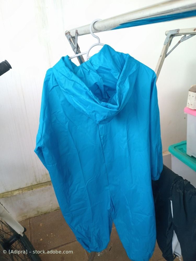 Ein blauer Overall hängt drinnen an einem Kleiderbügel; daneben befinden sich eine weiße Wand und Wäschestücke.